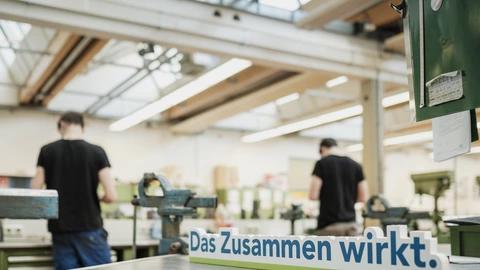 Auszubildende in der Werkstatt mit einem "Das Zusammen wirkt"-Schild im Vordergrund